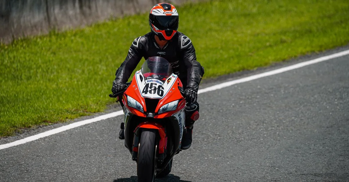 Motard en action courant sur un circuit asphalté sous la lumière du jour.