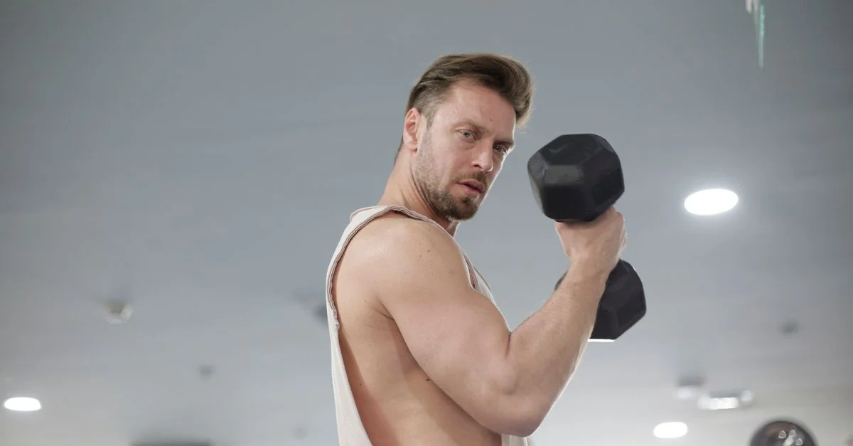 Hombre fuerte levantando mancuerna en el gimnasio, centrado en el culturismo y la fitness.