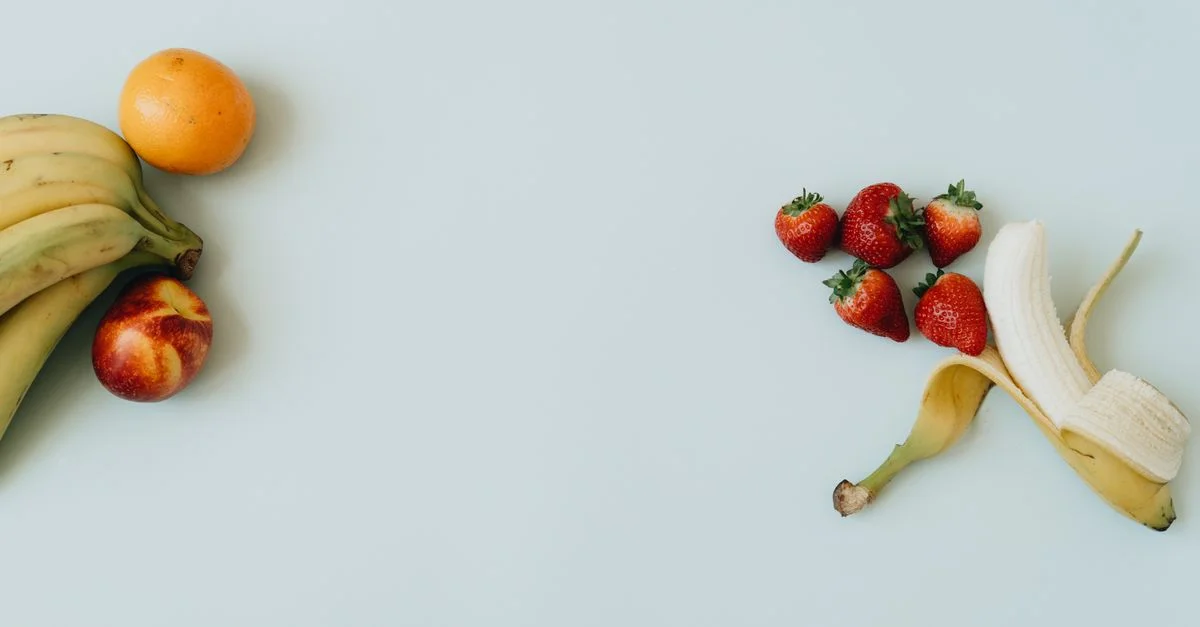 Frutas frescas variadas, incluyendo plátanos y fresas, sobre un fondo azul pastel.