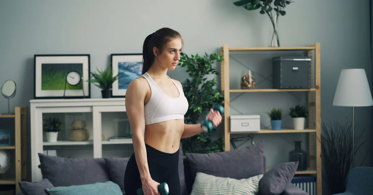 Mujer en forma, vestida con ropa deportiva, haciendo ejercicio con mancuernas en interiores.