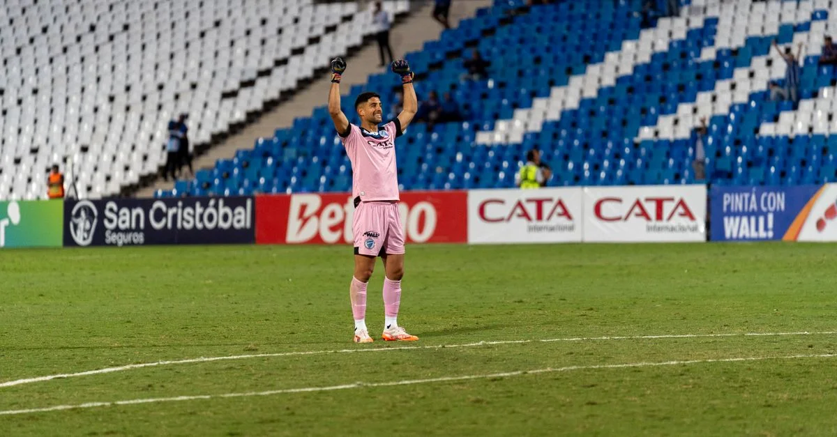 Portero de fútbol con camiseta rosa celebrando la victoria en el campo con los brazos levantados.