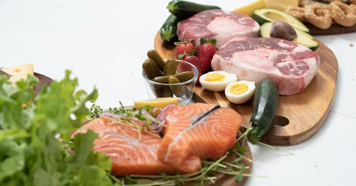 Ingredientes frescos variados keto, que incluyen salmón, carne de res y verduras en tablas de madera, perfectos para comidas saludables.