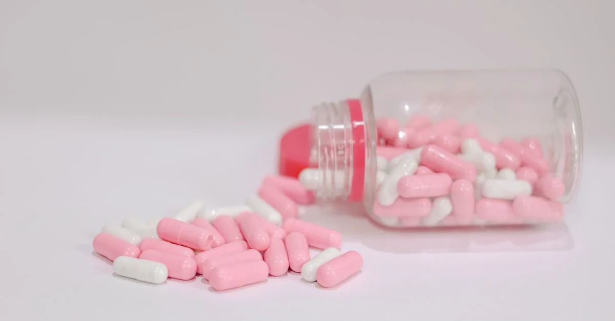 Primer plano de cápsulas de color rosa y blanco derramadas de una botella de plástico sobre un fondo blanco.