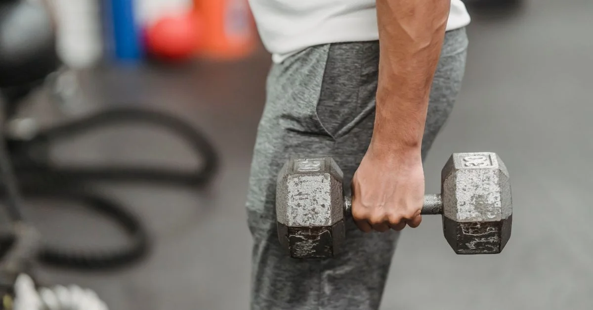 Un hombre sosteniendo una mancuerna en el gimnasio, centrado en el fitness y el entrenamiento de fuerza.