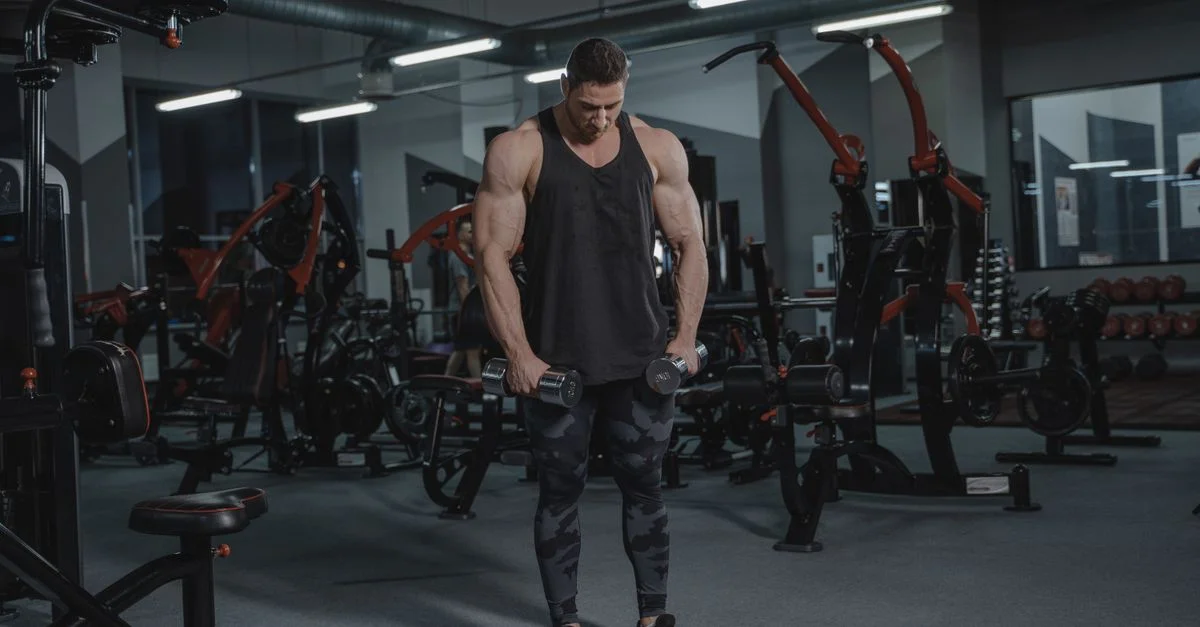 Hombre musculoso levantando mancuernas en un gimnasio moderno, demostrando fuerza y fitness.
