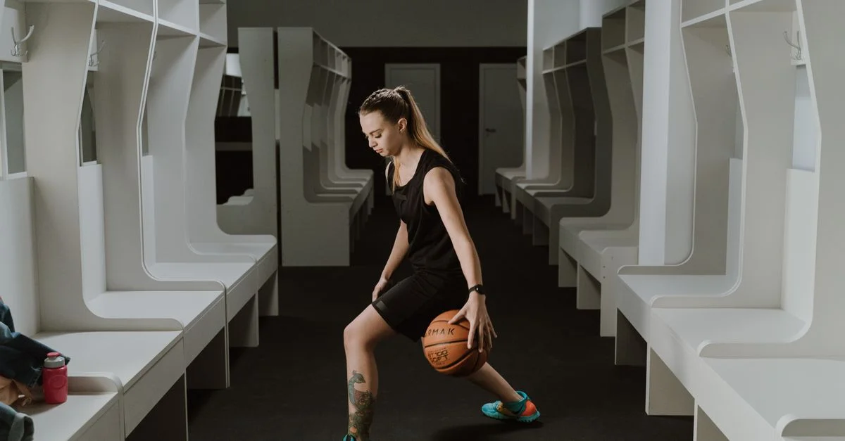 Una jugadora de baloncesto femenina practicando el dribbling en un vestuario moderno.