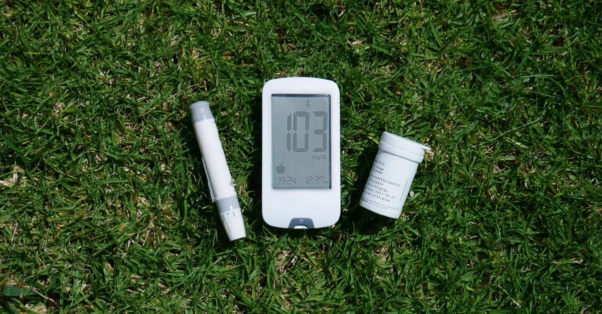 Herramientas para el manejo de la diabetes, incluyendo medidor de glucosa y tiras de prueba en la hierba, destacando el uso al aire libre.