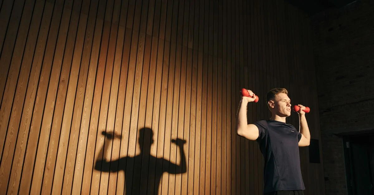 Hombre adulto haciendo ejercicio con mancuernas rojas en un gimnasio, mostrando fitness y un estilo de vida saludable.