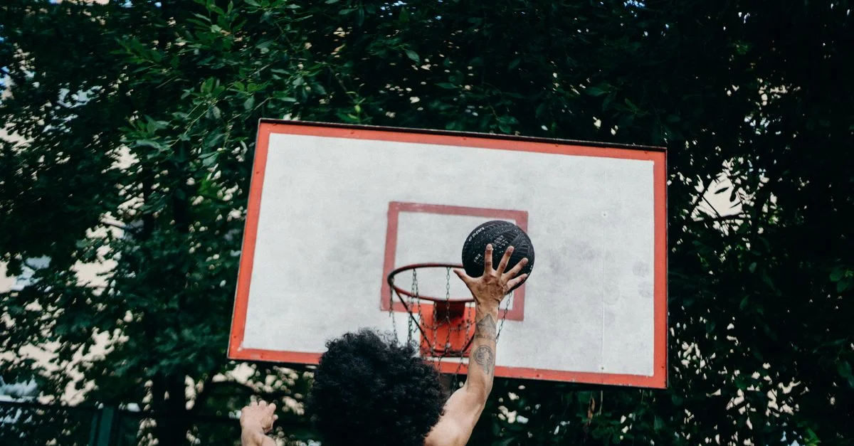 Un hombre haciendo una espectacular entrada de baloncesto en una cancha al aire libre durante el día.