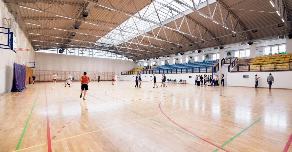 Vista en ángulo amplio de una cancha de baloncesto interior con jugadores practicando y participando en actividades deportivas.