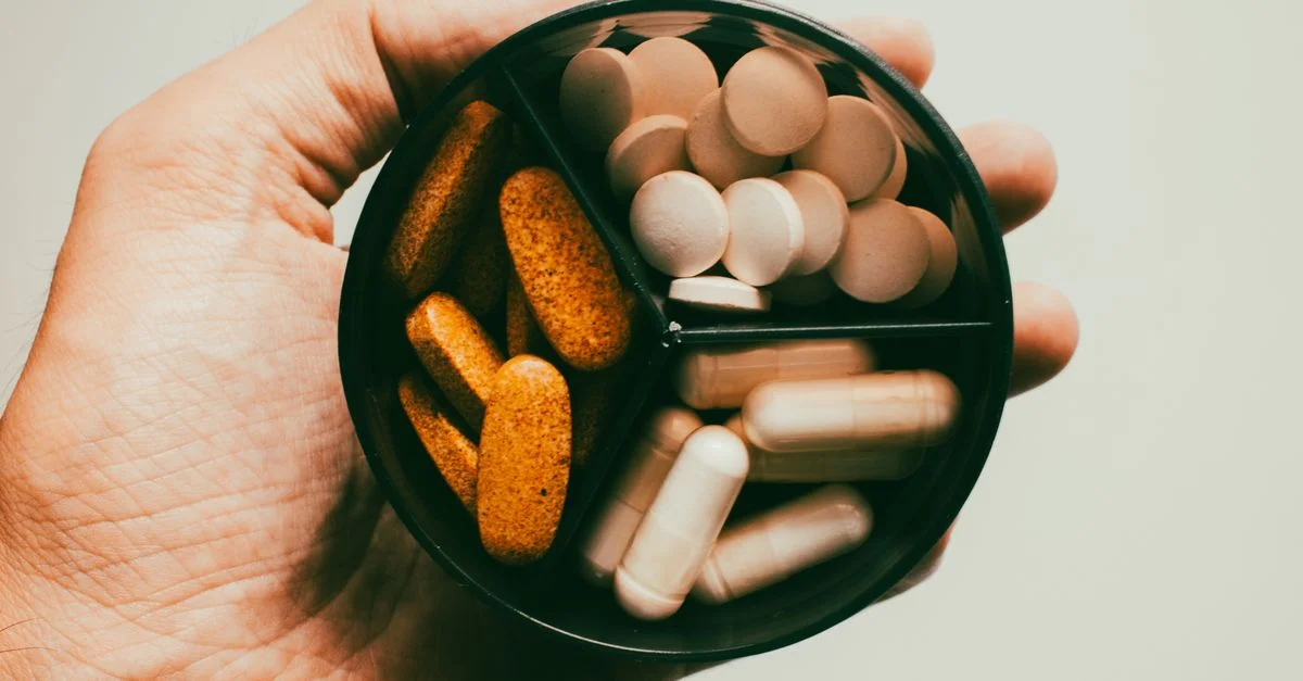 Primer plano de una mano sosteniendo diferentes tipos de suplementos y vitaminas.