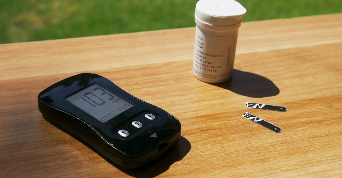 Medidor de glucosa en sangre y tiras de prueba sobre una mesa de madera a la luz del sol, representando el cuidado de la diabetes.