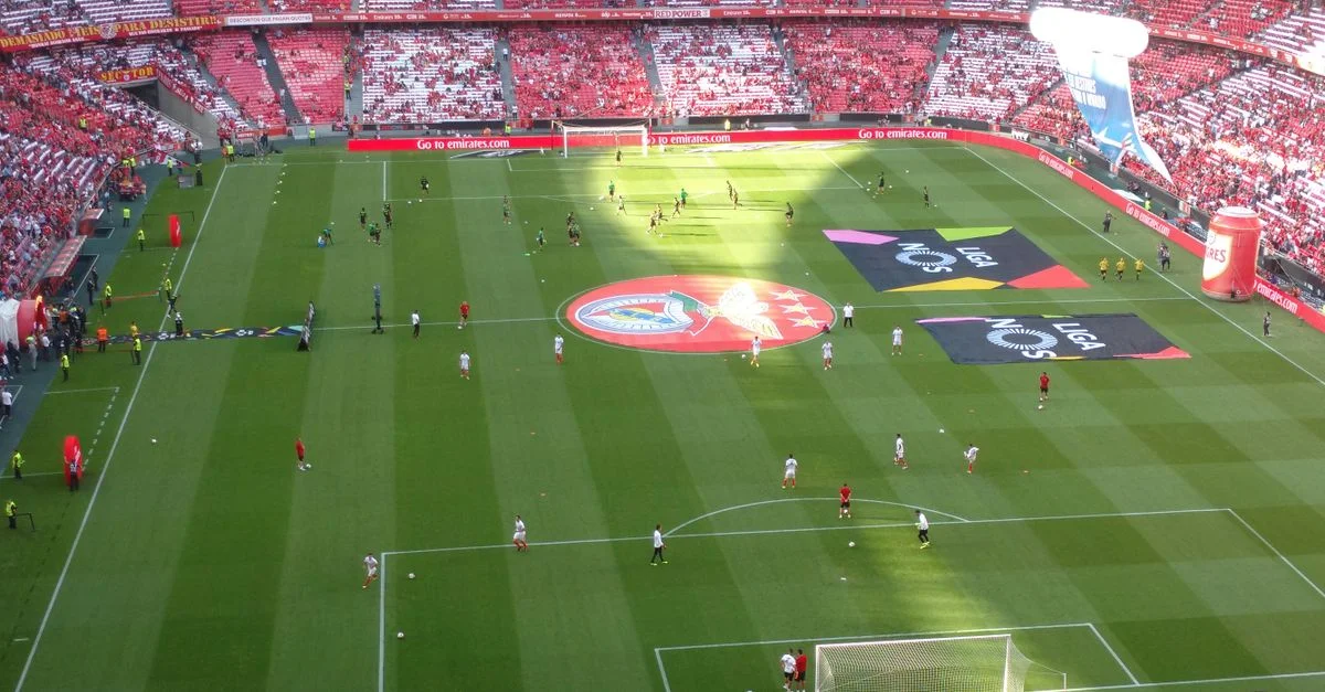 Vista aérea de un campo de fútbol durante un partido en un estadio lleno, con jugadores y aficionados.
