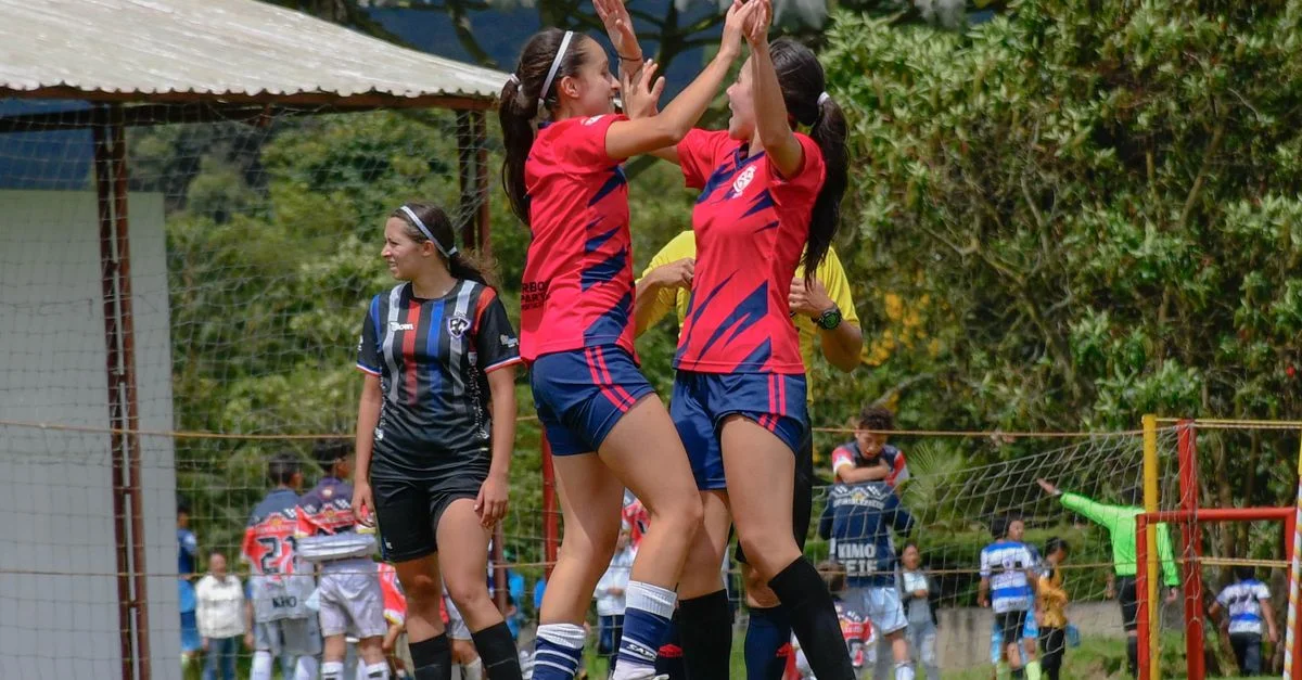 Jugadoras de fútbol femenino alegres celebrando después de un partido exitoso en un campo al aire libre.