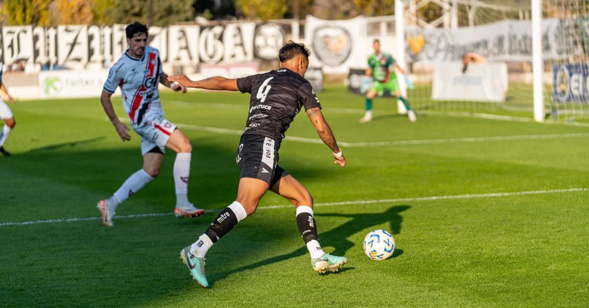 Jugadores de fútbol en intensa acción en un partido de un día soleado en un estadio al aire libre.