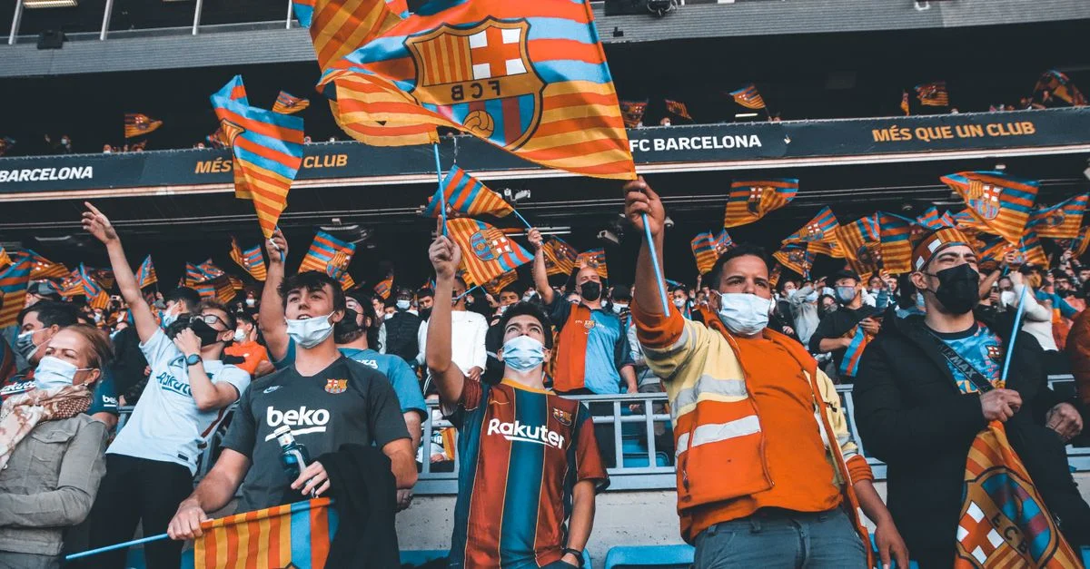 Los aficionados agitan entusiastamente las banderas del FC Barcelona en un partido de fútbol, mostrando espíritu de equipo y unidad.