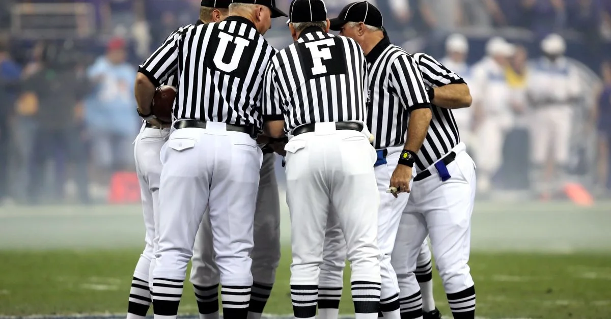 Grupo de oficiales deportivos en uniformes a rayas discutiendo en un campo de fútbol.