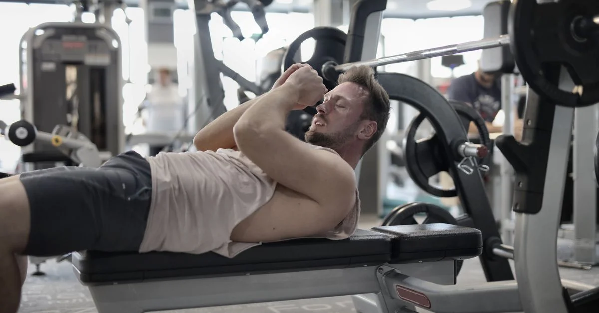 Un hombre descansando en un banco en el gimnasio, recuperando el aliento después de levantar pesas.