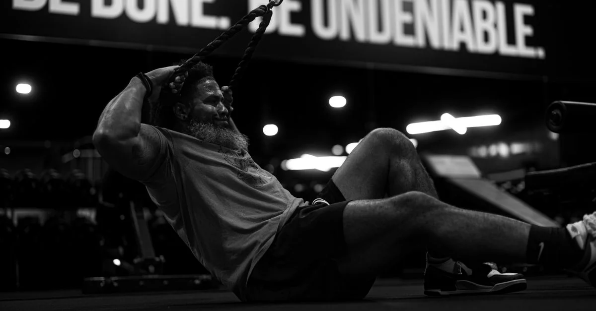 Foto en blanco y negro de un hombre realizando ejercicios intensos con cuerdas en un gimnasio, encarnando la determinación.