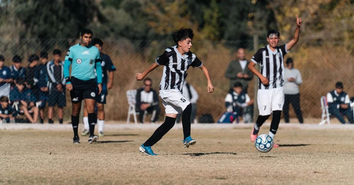 Jugadores de fútbol adolescentes en acción durante un partido competitivo al aire libre en un campo de césped.