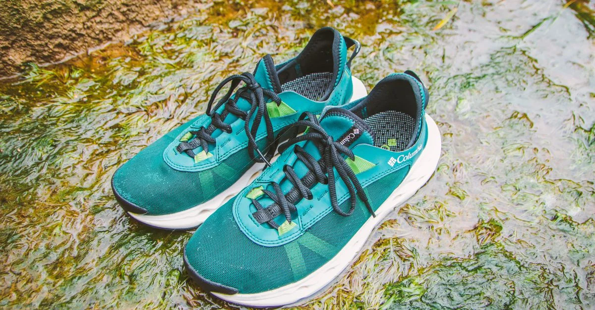 Par de zapatillas para correr de color verde azulado colocadas sobre una superficie húmeda y cubierta de musgo, resaltando la aventura al aire libre.