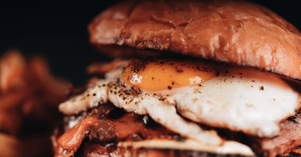 Deliciosa hamburguesa de carne cubierta con huevo frito y servida con patatas fritas, perfecta para amantes de la comida rápida.