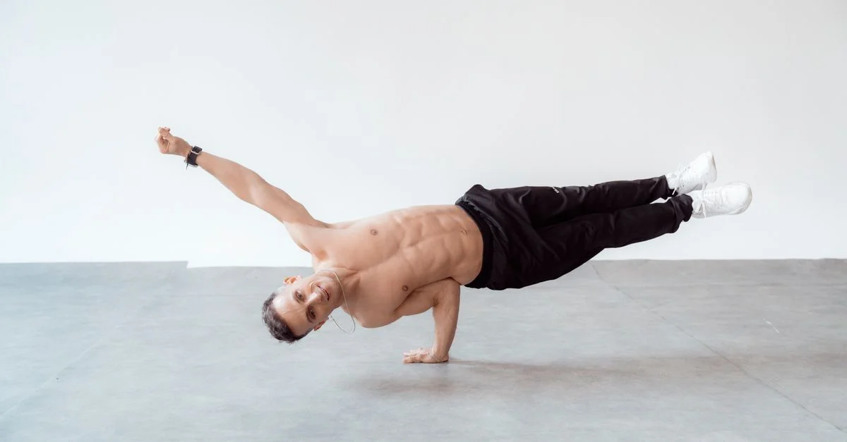 Un breakdancer masculin torse nu en pose de freeze à une main sur le sol d'un studio.