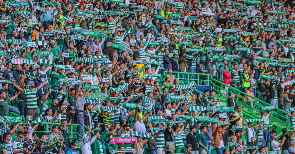 Multitud energética de aficionados al fútbol animando con bufandas en un estadio de Lisboa, Portugal.