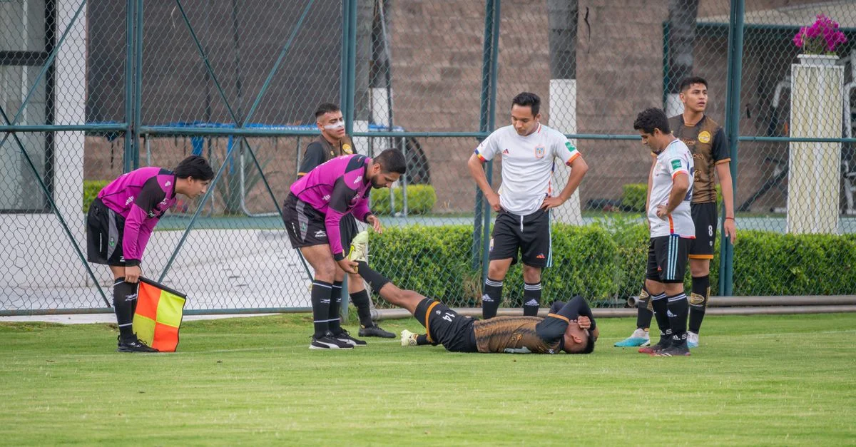 Jugador de fútbol lesionado en el campo con la ayuda de compañeros de equipo y árbitro en Texcoco, México.