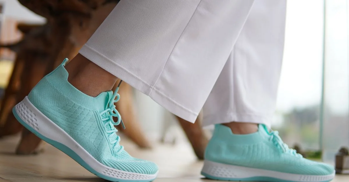 Zapatillas deportivas de color verde menta a la moda combinadas con pantalones blancos sobre un suelo de madera pulida: la combinación perfecta para un look moderno e informal.