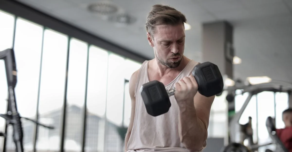 Hombre adulto concentrado en levantar una mancuerna durante una sesión de entrenamiento en el gimnasio.