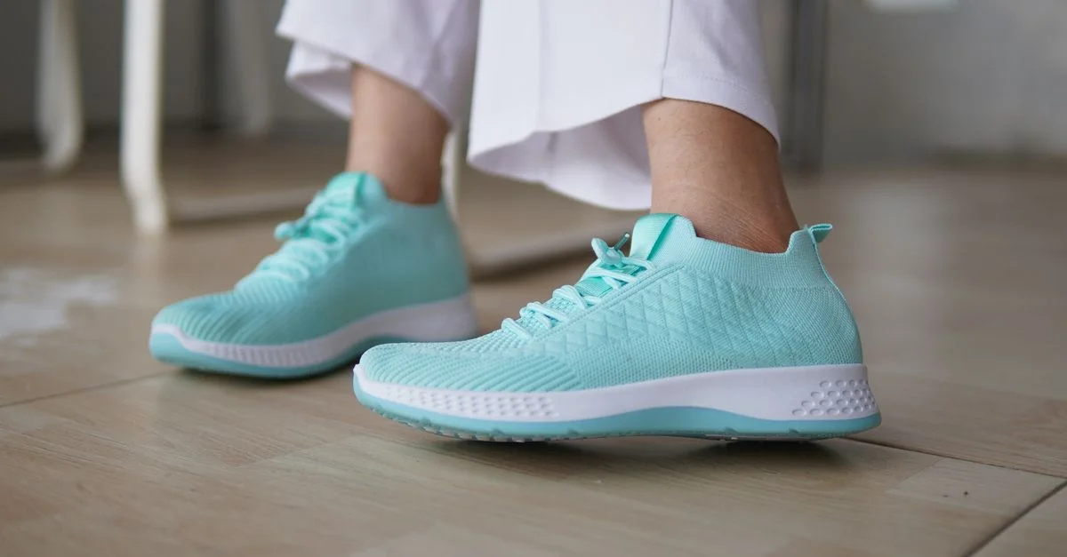 Zapatillas deportivas verde menta combinadas con pantalones blancos sobre un suelo de madera. Calzado moderno y elegante.