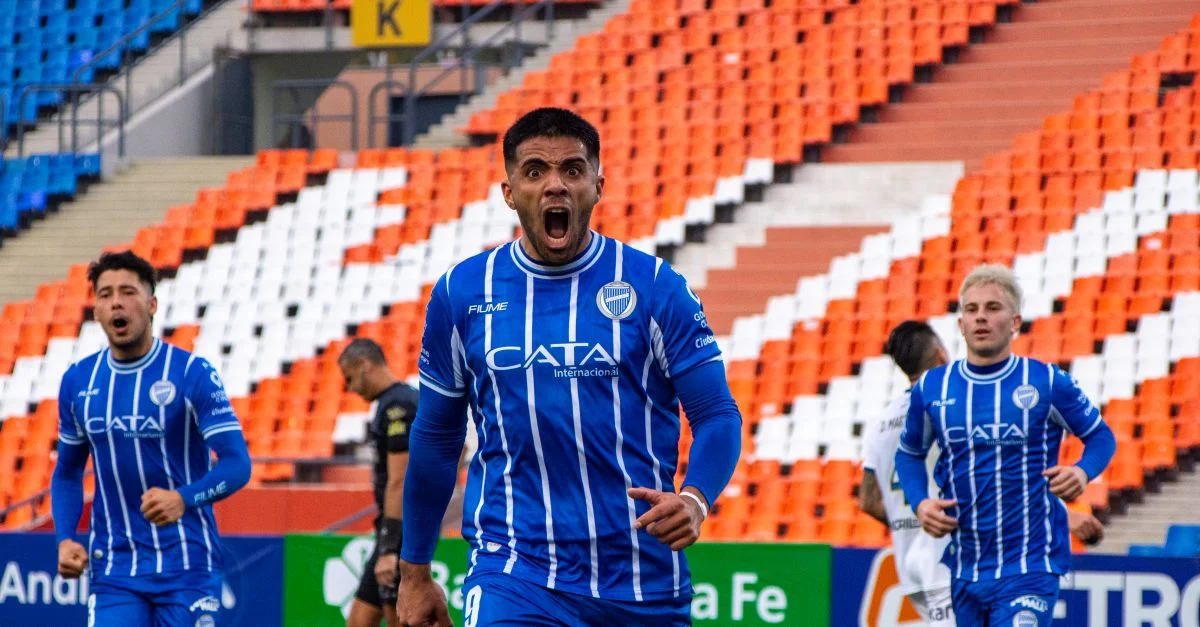 Jugadores de fútbol con camisetas azules celebran un gol en un estadio vacío.