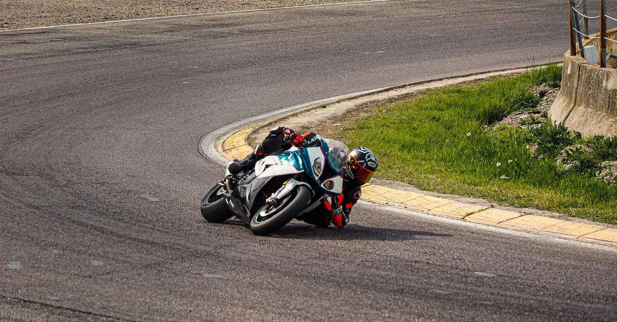 Un motocycliste aborde un virage serré sur une piste asphaltée lors d'une course de jour.