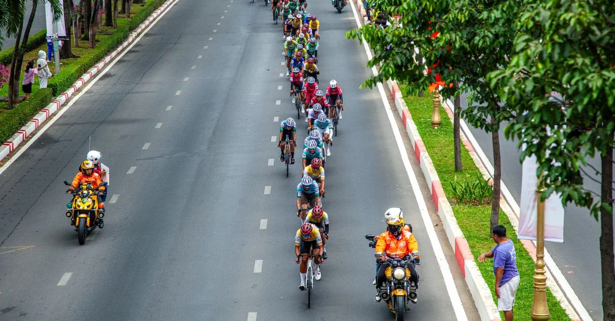 Vue aérienne d'une course cycliste sur route en ville, en journée, illustrant le travail d'équipe et la compétition.