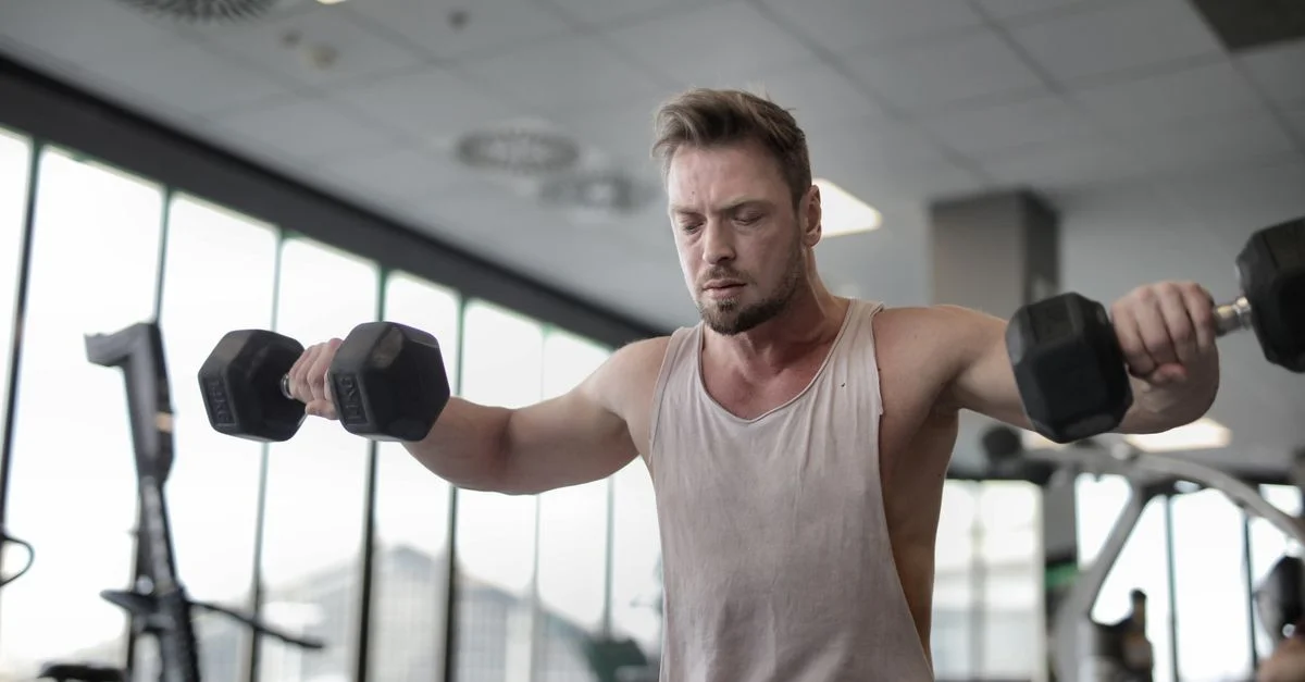 Hombre enfocado entrenando con mancuernas en el gimnasio, mostrando fuerza y determinación